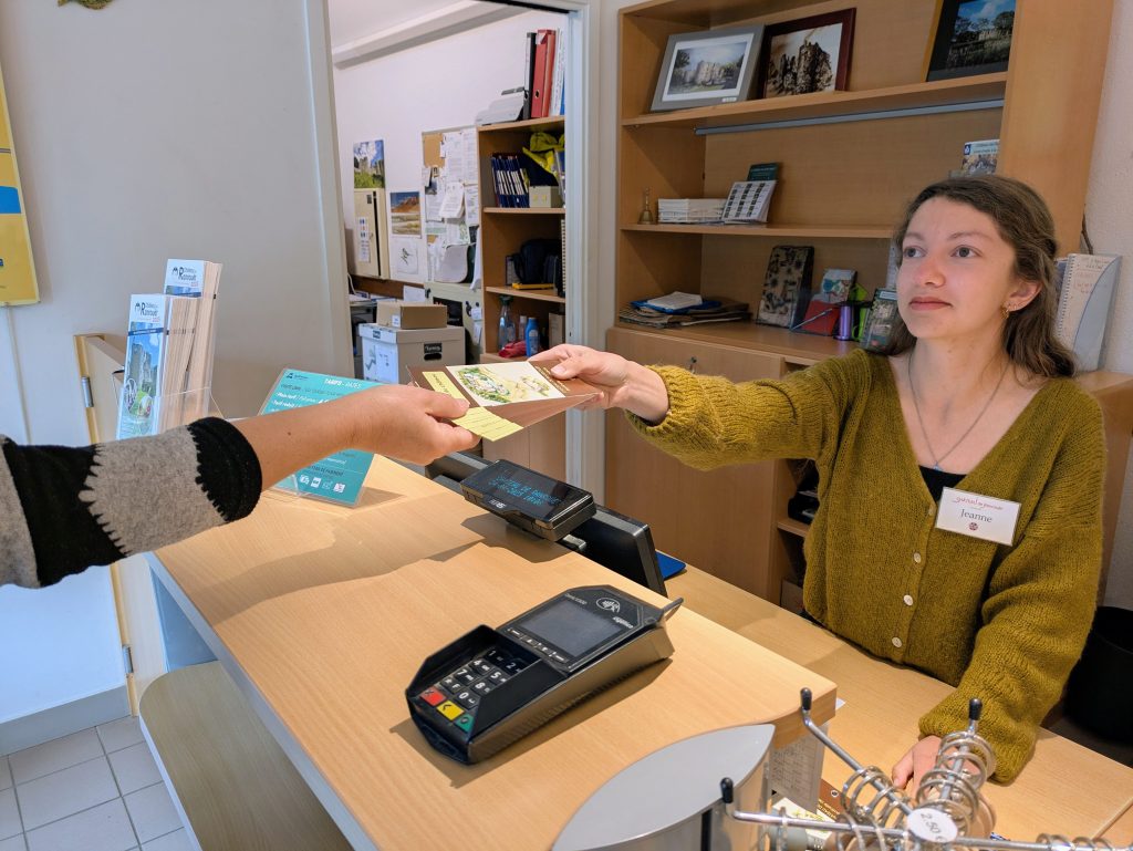 Médiatrice tendant un support de médiation à un visiteur à l’accueil du château.