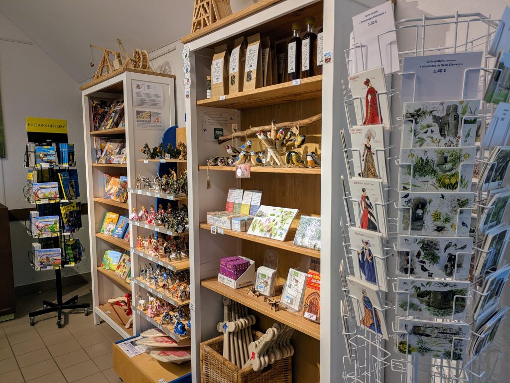 Boutique du château : trois commodes avec des livres, figures, épées et objets de décoration, et un présentoir avec des livres explicatifs.