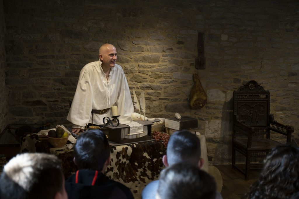 Spectacle en intérieur sur le thème de la table au Moyen Âge, avec un comédien devant une table remplie d’objets.