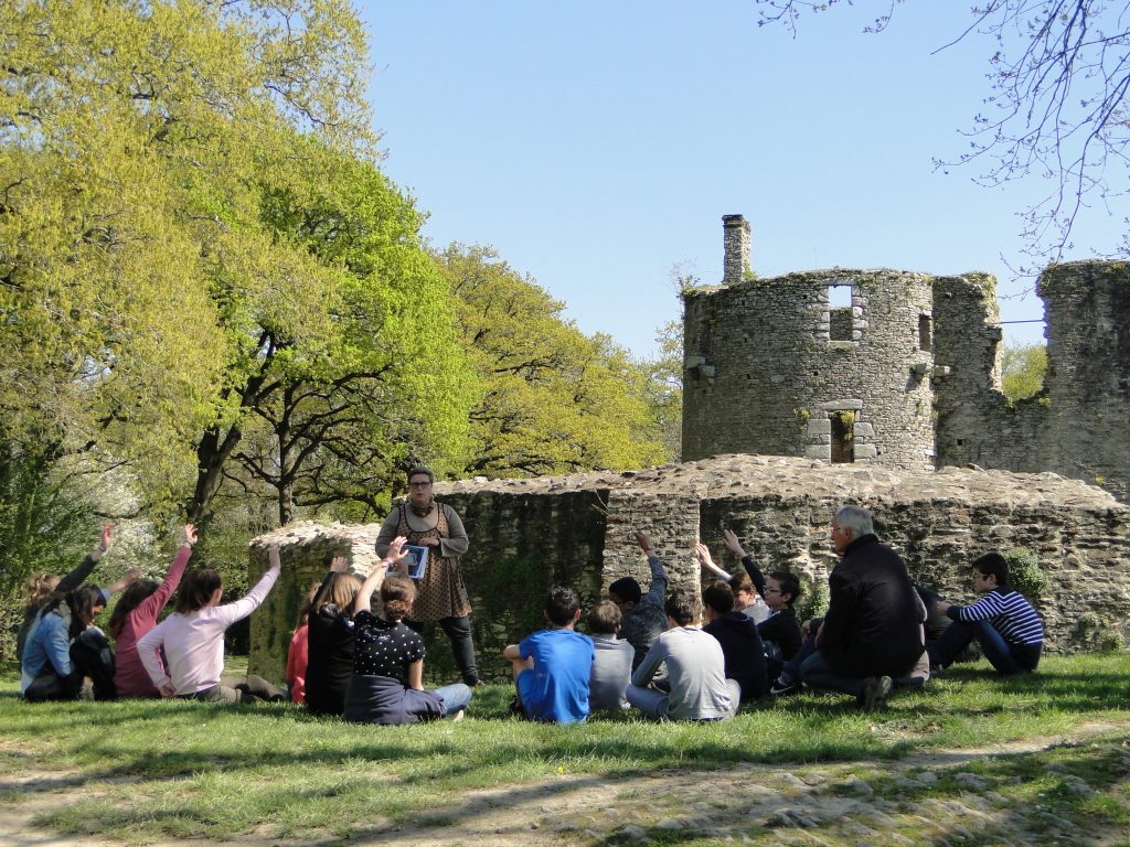 Un groupe d’enfants près des douves du château, écoutant la médiatrice.