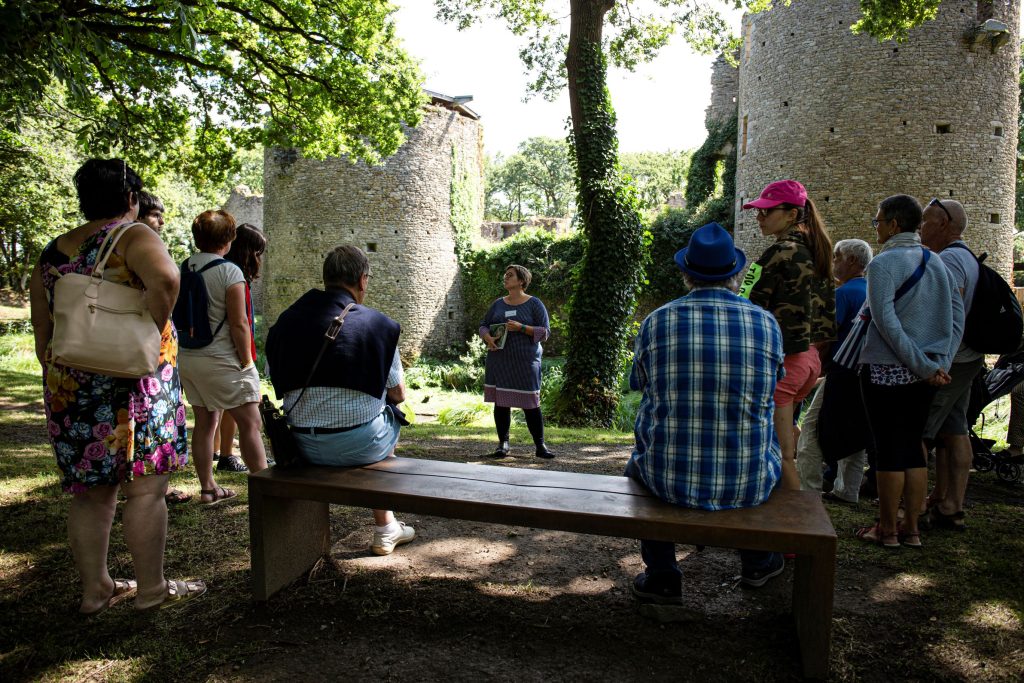 Un groupe de visiteurs rassemblés autour d’une médiatrice qui explique l’histoire du château autour des douves.